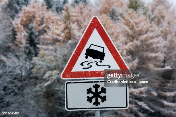 Traffic sign warning of packed snow on the street standing in front of a lightly snow-covered forest near the town of Lochen in Upper Bavaria,...