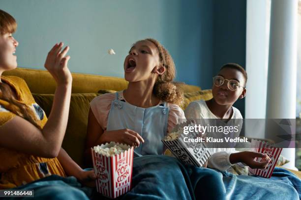 friends throwing popcorn and catching with mouth, at home - lanzar actividad física fotografías e imágenes de stock