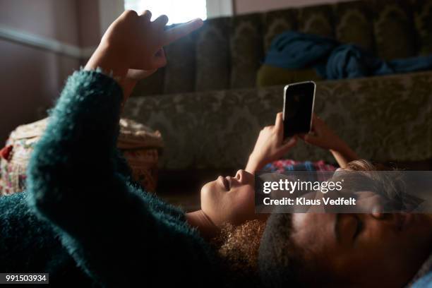 3 tween girls looking at their smartphones - lying on back girl on the sofa imagens e fotografias de stock