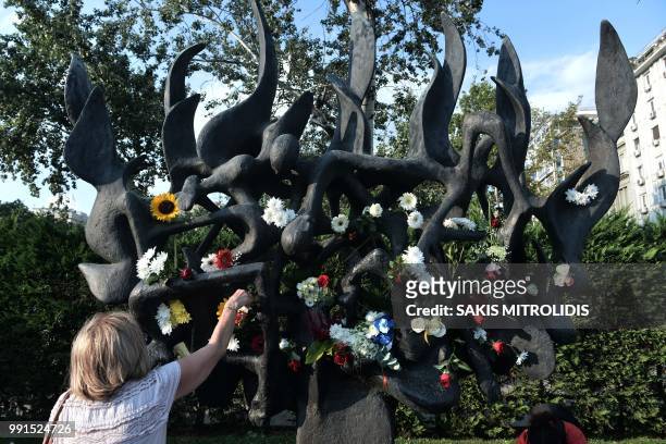 Woman puts a flower during a protest against the desecration of the Holocaust memorial in Thessaloniki on July 4, 2018. - Lats week vandals defaced...