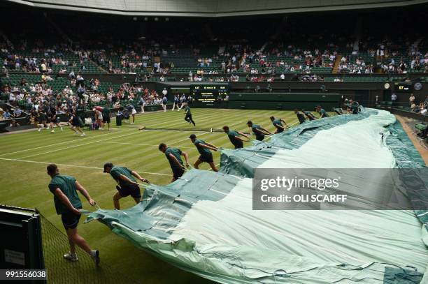 Groundstaff pull the covers over the grass court as rain stops play between Germany's Tatjana Maria and France's Kristina Mladenovic during their...