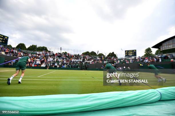 Groundstaff pull the covers over the grass as rain stops play between Switzerland's Stan Wawrinka and Italy's Thomas Fabbiano during their men's...