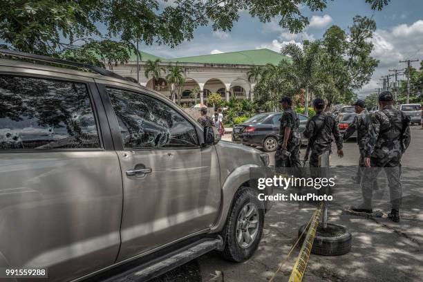 Heavily armed police officers walk past the bullet riddled vehicle of General Tinio Mayor Ferdinand Bote, who was assassinated by unidentified gunmen...