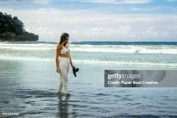 beautiful brunette woman walking on the shore of palawan beach while holding her slippers and looking downwards - puerto princesa stock pictures, royalty-free photos & images
