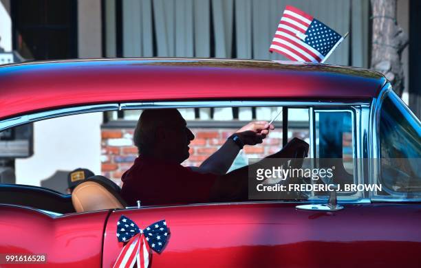 Man waves the US flag while driving his classic car during a Fourth of July parade in San Gabriel, California on July 4, 2018 as cities and towns...