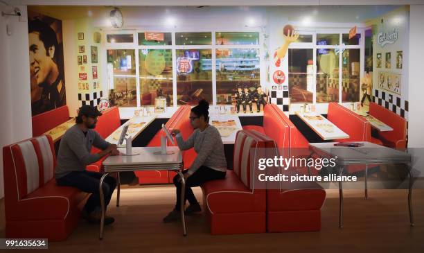 Two participants of a press conference sit in a reconstructed diner and inform themselves using tablets at the exhibition "The American Dream -...