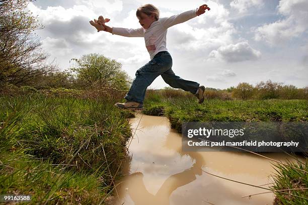 young girl leaping over stream - paul mansfield photography fotografías e imágenes de stock