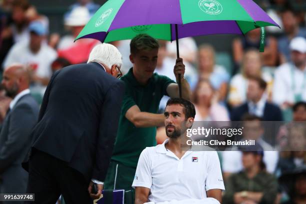 Marin Cilic of Croatia sits under an umberalla as it rains during his Men's Singles second round match against Guido Pella of Argentina on day three...
