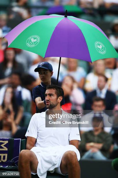 Marin Cilic of Croatia sits under an umberalla as it rains during his Men's Singles second round match against Guido Pella of Argentina on day three...