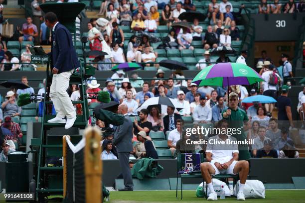 Marin Cilic of Croatia sits under an umberalla as it rains during his Men's Singles second round match against Guido Pella of Argentina on day three...