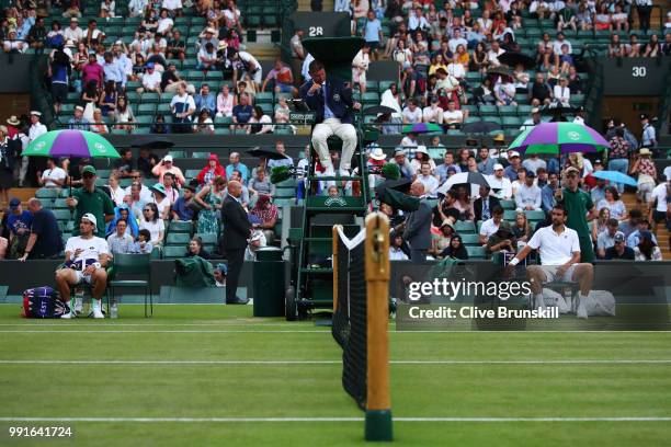 Guido Pella of Argentina and Marin Cilic of Croatia sit under umbrellas as it rains during their Men's Singles second round match on day three of the...