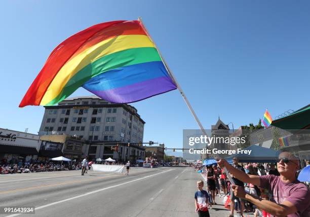 An LGBT supporter waves a pride flag as a float from the group "Mormon Building Bridges" passes by as part of the Provo Freedom Festival Parade on...