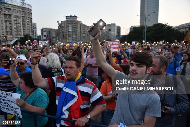 People hold up their smartphones as torches during a protest in front of the Romanian Government headquarters in Bucharest July 4, 2018. - Romania's...