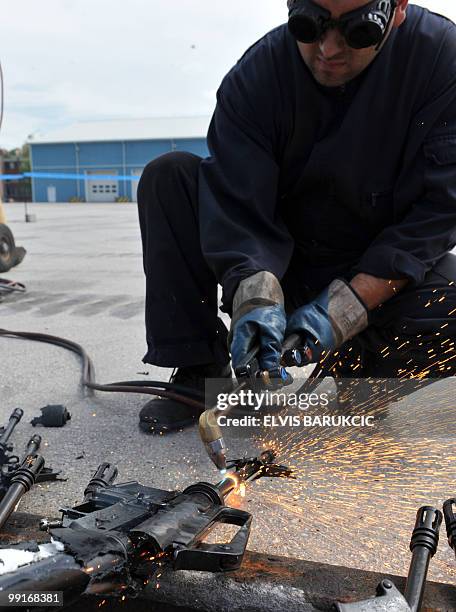 Bosnian workers uses an oxy-acetylene cutter to the barrel off a gun from the first of a batch of small arms scheduled for destruction at Base Camp...