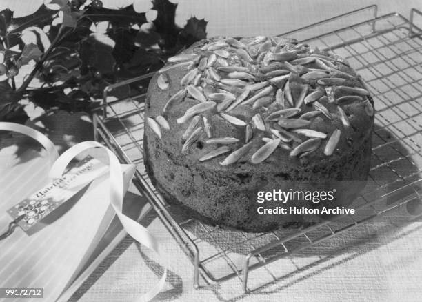 Rich Dundee Cake topped with almonds, next to a Yuletide greetings card, circa 1955.