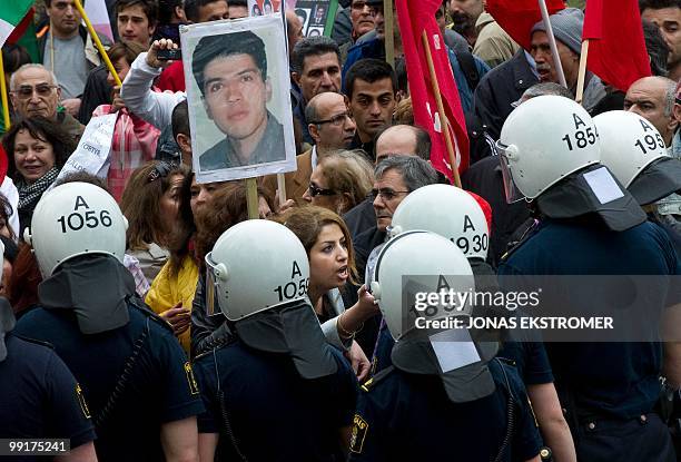 Demonstrators hold up the portrait of an unidentified Iranian as riot policemen watch outside the Iranian Embassy in Stockholm, on May 13, 2010...