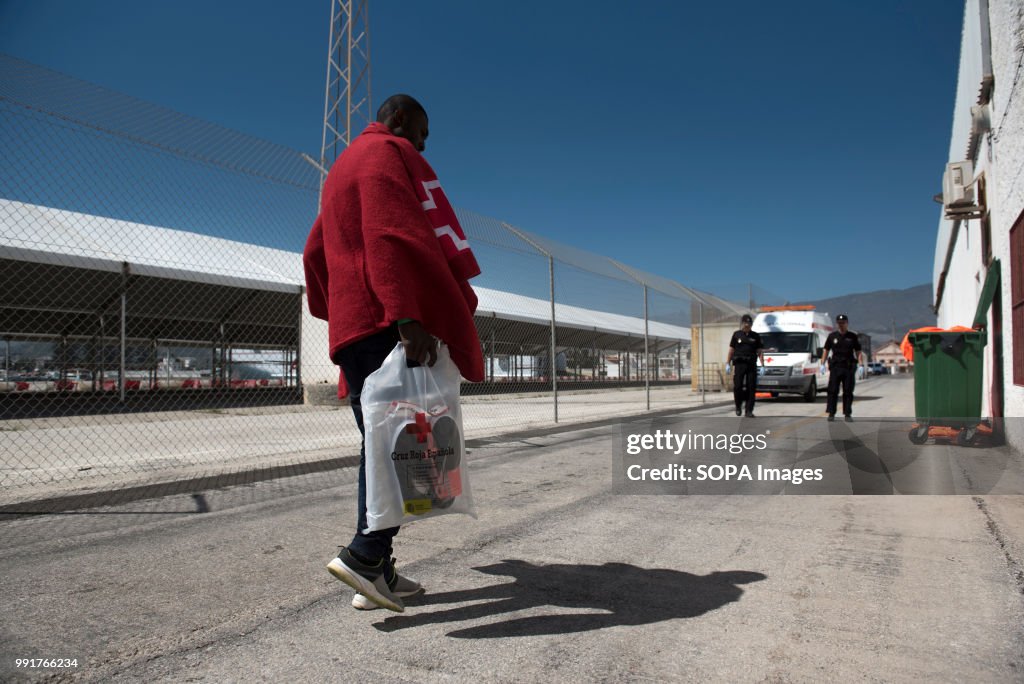 A migrant covered with a red blanket walks to the Red Cross...