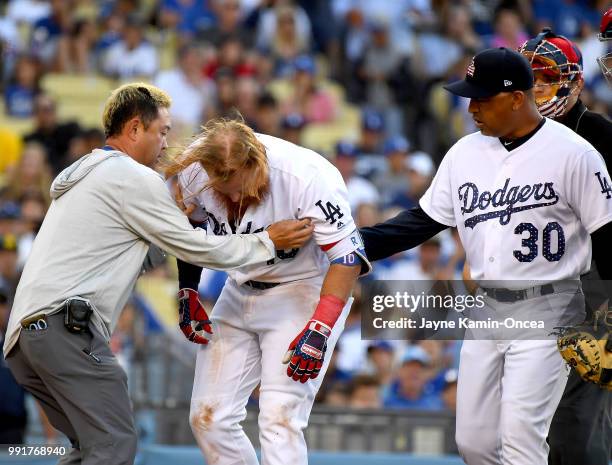 Justin Turner of the Los Angeles Dodgers is tended to by manager Dave Roberts and assistant athletic trainer Yosuke Nakajima after being hit in the...