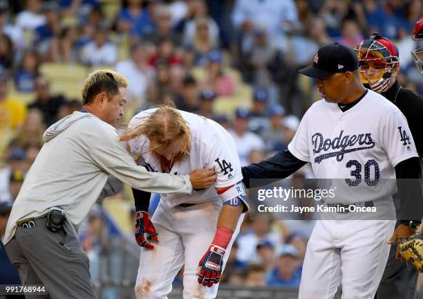 Justin Turner of the Los Angeles Dodgers is tended to by manager Dave Roberts and assistant athletic trainer Yosuke Nakajima after being hit in the...