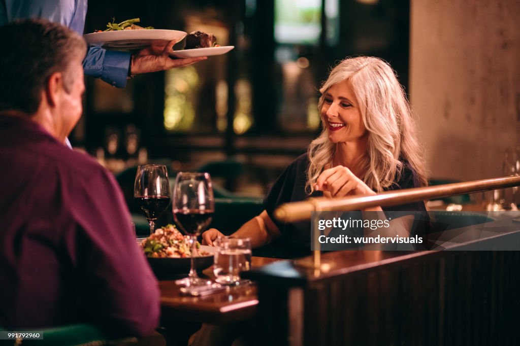 Waiter serving dinner to senior couple at fine dining restaurant