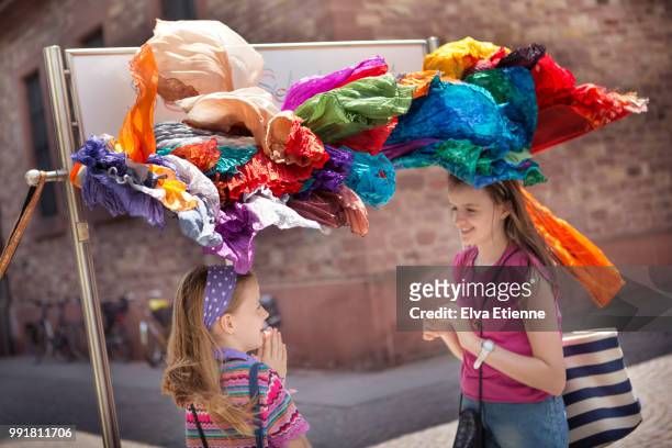 two smiling girls standing under a retail display rack of multi-coloured headscarves being blown in the wind - foulard vent photos et images de collection