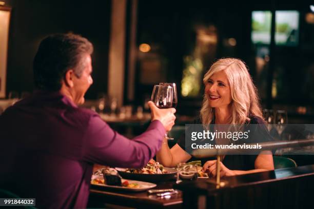 sorridente marito maturo e moglie che brindano con il vino a cena - fine dining foto e immagini stock