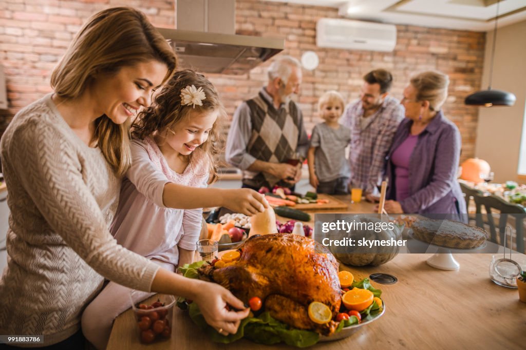 Happy mother and daughter preparing roasted turkey for Thanksgiving dinner.