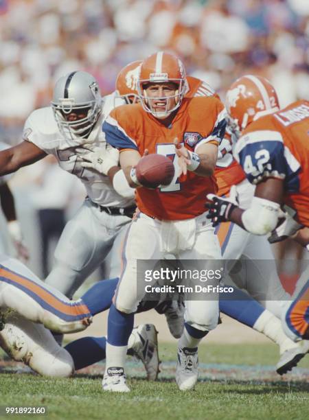 John Elway, Quarterback for the Denver Broncos hands the ball off to his running back Leonard Russell during the American Football Conference West...