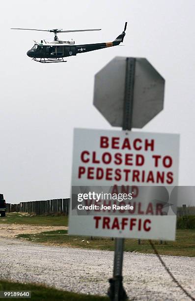 Military helicopter flies past a beach closed sign after what appeared to be small oil globs washed ashore at Fourchon Beach as efforts continue to...