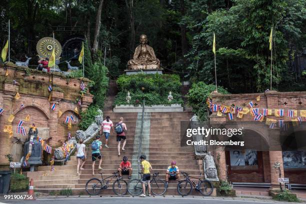 Cyclists sit as tourists walk up a flight of stairs at Wat Phra That Doi Suthep in Chiang Mai, Thailand, on Wednesday, July 4, 2018. Photographer:...
