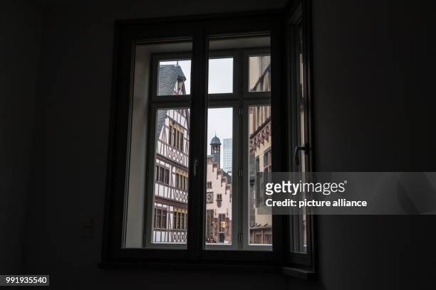 The view through the window shows the historic town hall and houses with reconstructed historic fronts in the old town centre of Frankfurt, Germany,...