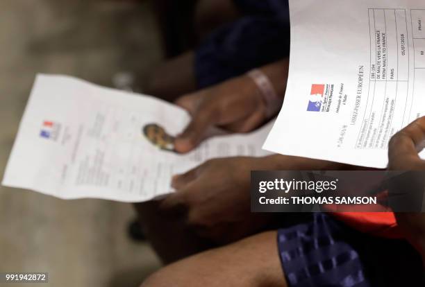 Migrants sit holding their official 'Laissez-Passer Europeen' papers as they wait in the immigration hall at Roissy-Charles de Gaulle airport on the...