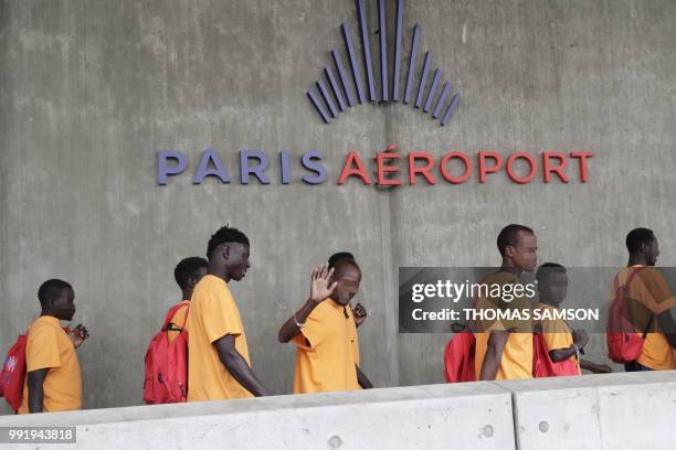 Migrant waves as he and others leave the immigration hall at Roissy-Charles de Gaulle airport on the outskirts of Paris, to a waiting bus on July 5...