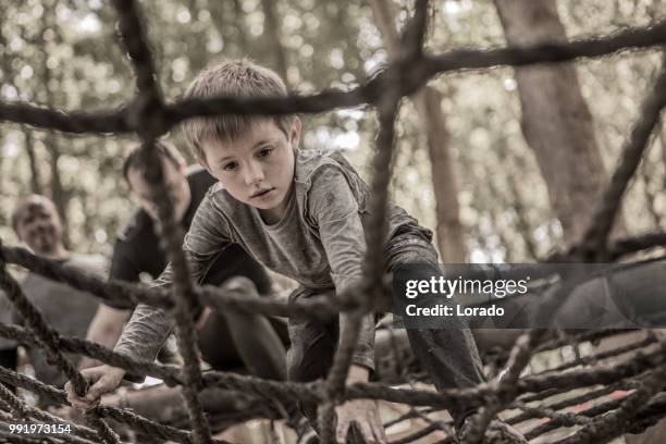 bambino maschio pre-adolescente individuale che si diverte sportivamente su un ponte di corda in un percorso ad ostacoli pubblico di corsa al fango - scala di corda foto e immagini stock