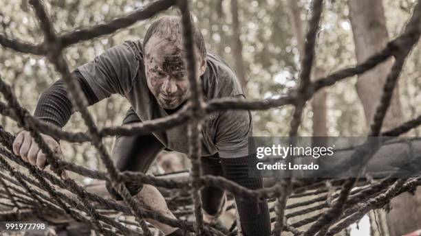 uomo individuale che si diverte sportivamente su una scala di corda in un percorso ad ostacoli pubblico di corsa al fango - scala di corda foto e immagini stock