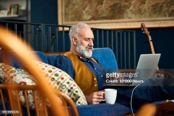 senior man working on laptop at home with serious expression - old wise business man white stock-fotos und bilder
