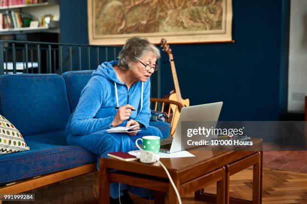 senior woman using laptop and making notes - confused writing stock-fotos und bilder