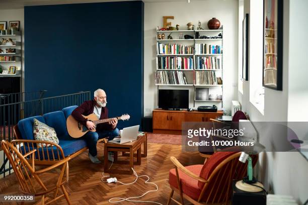 senior man practising guitar at home in retro living room - learn guitar stockfoto's en -beelden