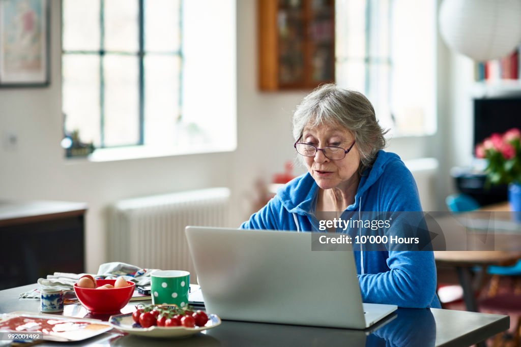 Senior woman wearing glasses using laptop at home