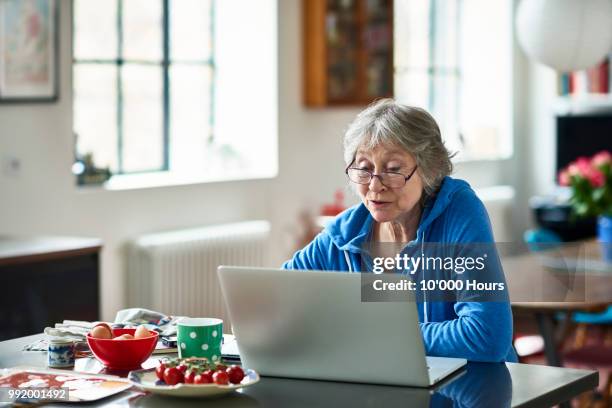 senior woman wearing glasses using laptop at home - senior using computer stock pictures, royalty-free photos & images