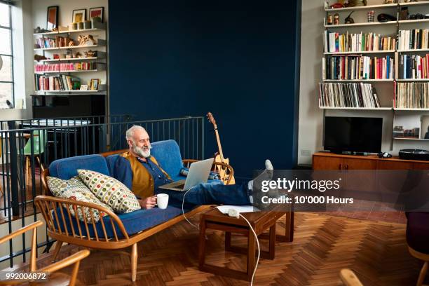 senior man using laptop in retro style living room - man living room stockfoto's en -beelden