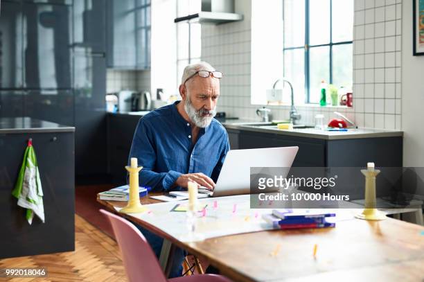 hipster senior man using laptop with map on table - bildserie stock-fotos und bilder