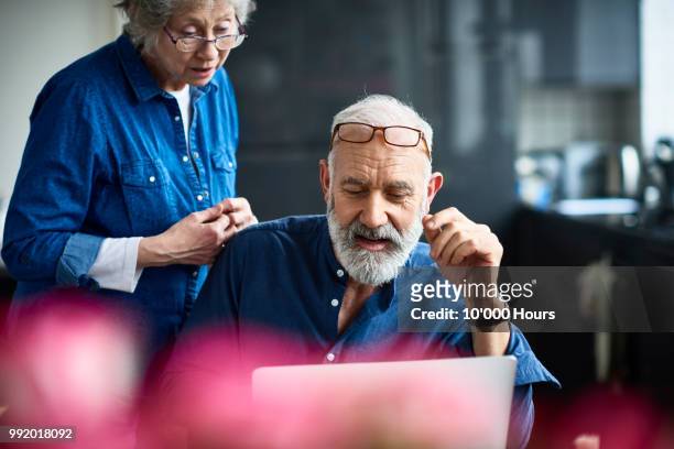 hipster senior man with beard using laptop and woman watching - pensionamento foto e immagini stock