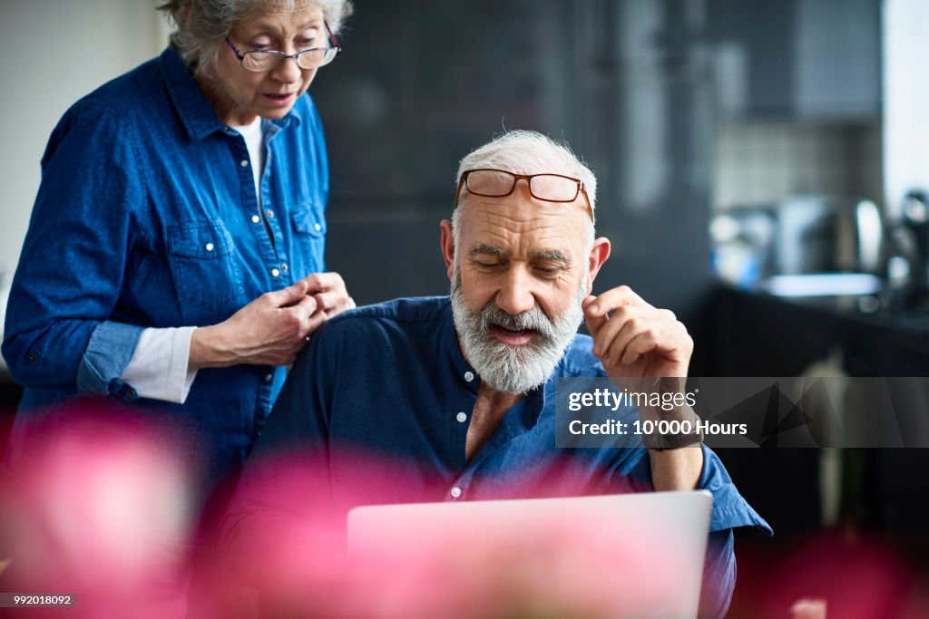 Hipster senior man with beard using laptop and woman watching