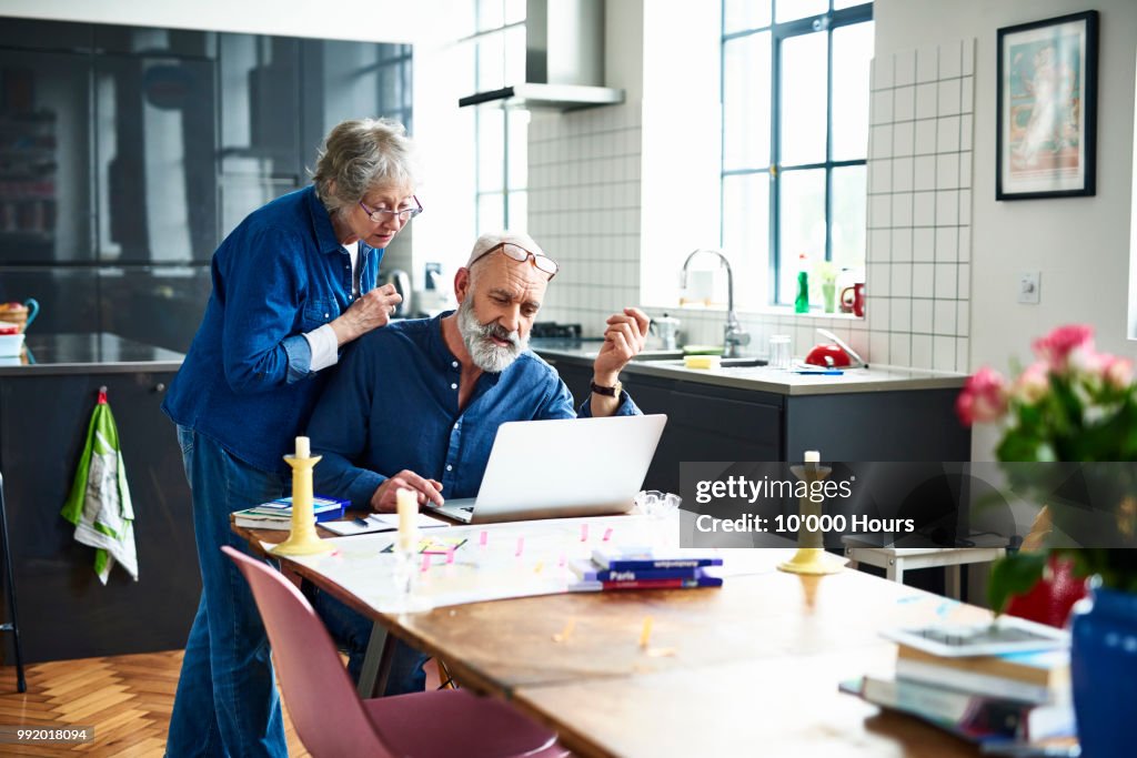 Senior couple planing vacation with map and laptop on table