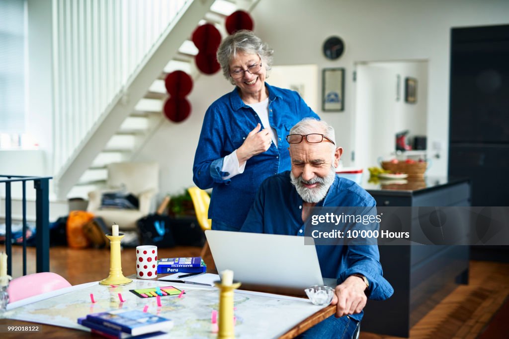 Cheerful retired couple at home planning vacation and man using laptop