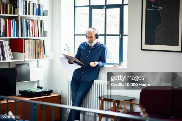 cool looking senior man in apartment listening to vinyl record - hipster candid stockfoto's en -beelden