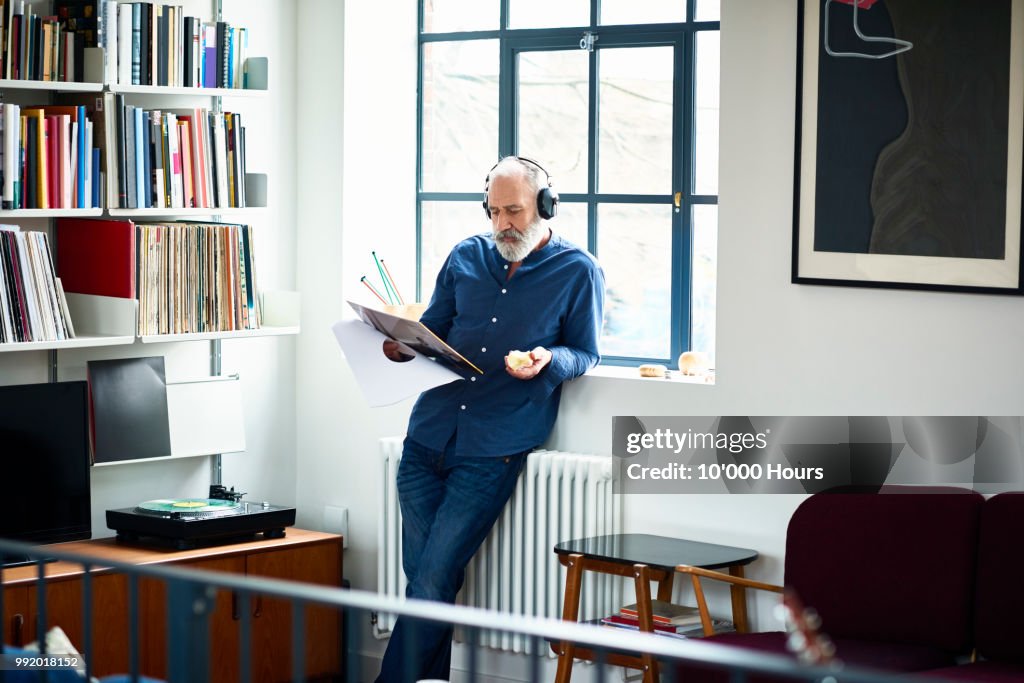 Cool looking senior man in apartment listening to vinyl record