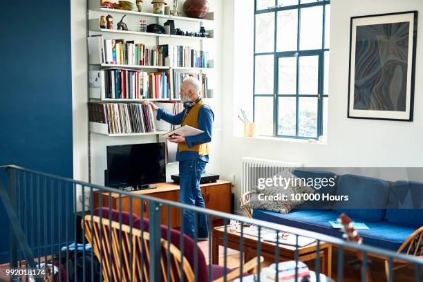 senior man sorting through his record collection in living room - organised shelves imagens e fotografias de stock