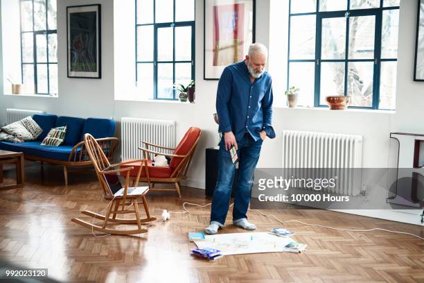 senior man in apartment looking at map laid out on parquet floor - hours around the world stock pictures, royalty-free photos & images